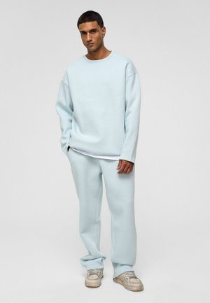 Lichtblauwe fleece sweatshirt en bijpassende joggingbroek, beide met een ontspannen pasvorm. Gestructureerde stof, ribgebreide manchetten en een lagen witte shirt eronder.