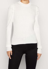 Pull blanc côtelé à manches longues et col rond. Présente des détails froncés sur les coutures des épaules et des poignets ajustés.