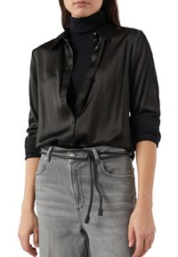 Czarna jedwabna koszula z klasycznym kołnierzykiem i zapięciem na guziki z przodu, zestawiona z szarymi spodniami jeansowymi, wyposażonymi w pasek z ozdobnym sznurkiem.