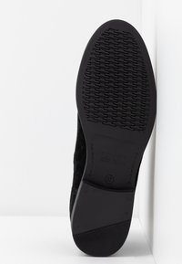Semelle de chaussure en suede noir avec une surface en caoutchouc texturé. Présente un logo en relief et la taille '37' sur le côté. Design plat avec un bout arrondi.