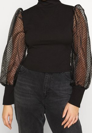 Schwarzer Rollkragenpullover mit durchsichtigen, voluminösen, gepunkteten langen Ärmeln, kombiniert mit hoch taillierten schwarzen Jeans.