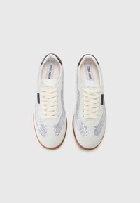 White sneakers with silver sequined side panels, beige accents, round toe, and beige laces. Rubber sole with a textured finish.