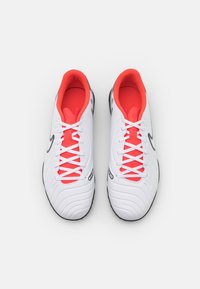 White soccer cleats with textured design, bright red accents on the interior and laces, and a black sole. Features a sleek shape and profile.