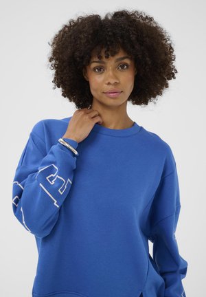 Hanorac albastru cu mâneci lungi, inscripție albă pe brațul stâng, realizat dintr-un material moale din bumbac amestecat. Design clasic cu guler rotund.