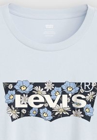 Ανοιχτό μπλε μπλουζάκι με γραφικό σχέδιο από λουλούδια σε μπλε και λευκό, πάνω σε σκούρο ναυτικό φόντο. Διαθέτει εμφανώς το λογότυπο "Levi's".