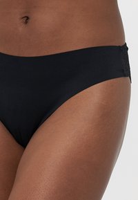 Black bikini bottom made of smooth fabric, featuring a lace accent on the left side. High-cut design with a seamless waistband.