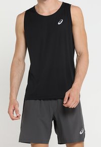 Muž v černém bezrukávovém sportovním tričku a šedých sportovních šortkách, oba s bílým logem Asics na levé straně.