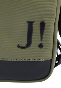 Borsa verde oliva con superficie testurizzata, caratterizzata da un logo in rilievo nero ben visibile "J!" e una sezione inferiore nera.