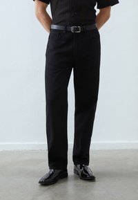 Black denim pants with a straight-leg cut, featuring front pockets and a classic design. Worn with a black belt and shiny black shoes.