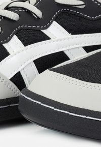 Gros plan des détails d'une sneaker noir et blanc montrant un tissu texturé, des lacets blancs et des accents en cuir cousus sur la semelle et les côtés.