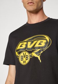 Mand med sort t-shirt med stort gult Borussia Dortmund BVB 09 og Puma logo på brystet, kortet ved hals og arme.
