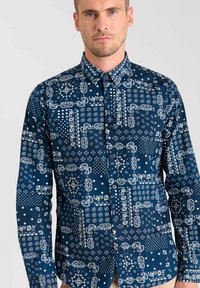 Marineblauw blouse met knopen, voorzien van ingewikkelde witte patronen, waaronder sterren en bloemmotieven, met een klassieke kraag en lange mouwen.