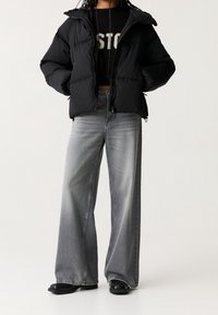 Sort pufferjakke med en cropped design, der har quiltede sektioner og hætte. Båret med slidte grå jeans med vidde og sort fodtøj.