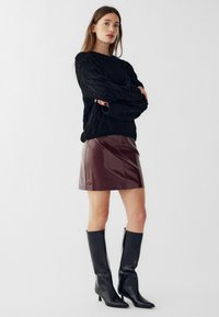 Črn pulover z pletenjem in ohlapnim krojem, sijoča bordo mini krilo in črne usnjene škornje do kolen s koničastimi nosovi in petami.