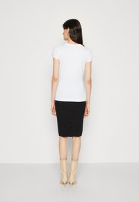 Hvid kortærmet top kombineret med en sort pencil skirt med slids. Modellen har beige hæleboots på. Baggrunden er ensfarvet hvid.