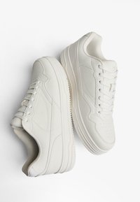 Bijele tenisice s glatkim kožnim gornjim dijelom, perforiranim prstima, ravnim vezicama i debelim gumiranim potplatom. Minimalistički dizajn s suptilnim detaljima šavova.