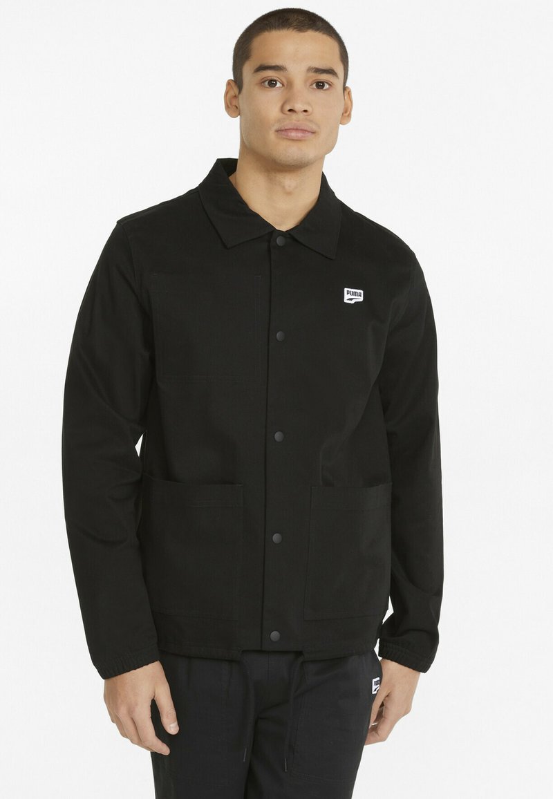 Giubbotto nero con colletto, bottoni a pressione, due tasche frontali e un piccolo logo del marchio sul petto a sinistra. Tessuto dalla trama liscia.