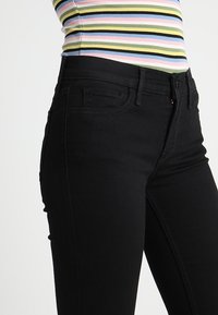 Vaqueros de mezclilla negra con un corte slim, diseño de cinco bolsillos y cierre de cremallera. Presentan costuras en contraste y una textura suave.