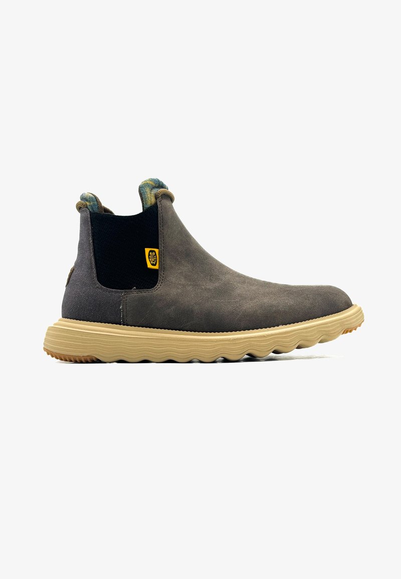 Bottines en suede marron avec un panneau élastique noir, tirant texturé au talon et semelle en caoutchouc beige avec un motif ondulé et une étiquette logo.