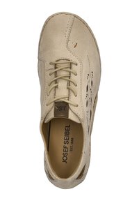 Vaaleanbeige nahkakengät, joissa on rei'itettyjä yksityiskohtia, pyöreä kärki ja nauhakiinnitys. Sisäpuolella on ruskea vuori, jossa näkyy brändin logo.