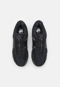 Melni Nike Vomero 5 apavi ar acu tīklu augšdaļu, strukturētiem pārklājumiem un kontrastējošām pelēkām šņorēm. Ikonisks logotips uz mēles; izturīga gumijas zole.