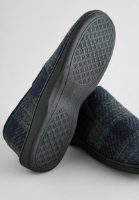 Uldeslippers med et mørkeblåt og gråt ternet design, gummisåler med et struktureret mønster, og slip-on design uden snørebånd.