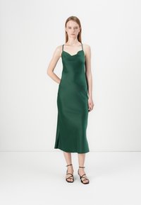 Rochie satin verde, cu decolteu înerve, design de lungime medie, bretele subțiri ajustabile și o tăietură laterală. Asortată cu sandale negre cu curele.
