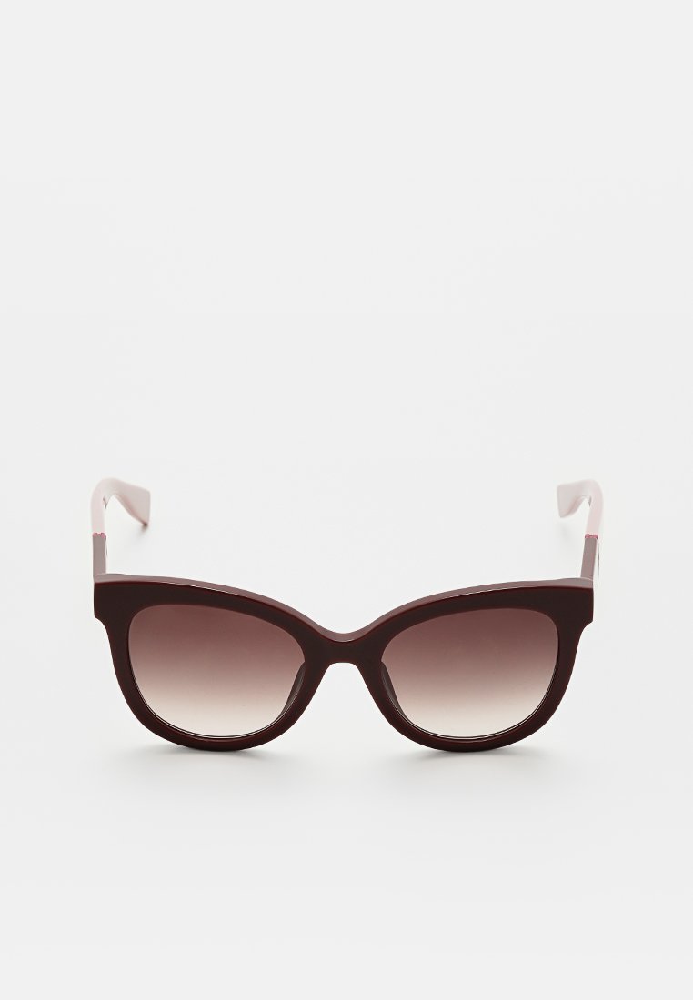 Lunettes de soleil en forme d'yeux de chat avec une monture bordeaux et des verres dégradés. Présente une texture lisse, des branches effilées et des accents matériels minimaux.