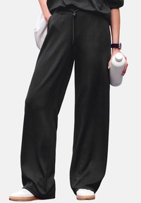 Platas kājstarpes melnas sporta bikses, izgatavotas no mīksta auduma, ar elastīgu jostasvītnes un auklu. Saskaņotas ar baltām sporta apaviem un ūdens pudeli.