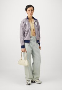 Lilla zip-up jakke med marineblå detaljer, beige ribbet crop topp, lyseblå vide bukser og kremfarget håndveske. Grå og hvite sneakers.