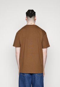 Camiseta de algodón marrón con mangas cortas y cuello redondo, con un corte holgado y una textura suave. Diseño liso, sin patrones.