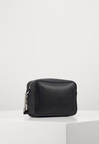 Sort lædertaske med rektangulær form, tekstureret overflade, sølvfarvet kædestrop og lynlås lukning, der har et minimalistisk design.