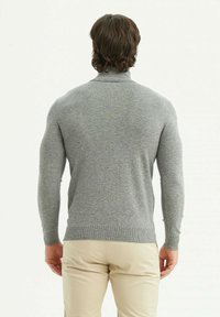 Pull en tricot gris avec des manches longues, un col montant et un ourlet côtelé, présenté de dos sur un fond clair.