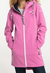 Rosa softshell-jacka med en vit dragkedja, två framfickor, justerbar huva och svart inre foder. Har dragsko med trädetaljer.