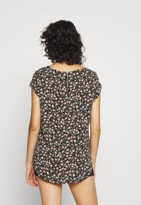 Sorte blomster bluse med korte ærmer, en rund nederkant og en lynlåsdetaile på ryggen. Små lyserøde og hvide blomster er spredt over hele blusen.