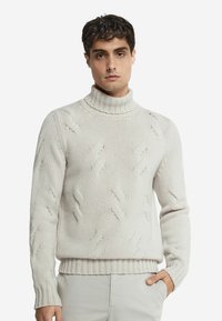 Ljusbeige stickad tröja med hög ribbad krage, som har ett strukturerat mönster och ribbade ärmslut och nederkant. Tillverkad av ett mjukt tyg.