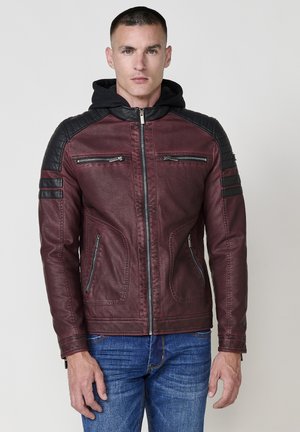 Giacca di pelle rossa con spalle imbottite nere, due tasche sul petto con zip e tasche laterali. Presenta un cappuccio e dettagli di cucitura a contrasto.