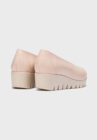 Zapatos de piel de color rosa claro, tipo slip-on, con una textura suave y una suela de cuña gruesa en color beige, que presenta surcos horizontales para mayor agarre.