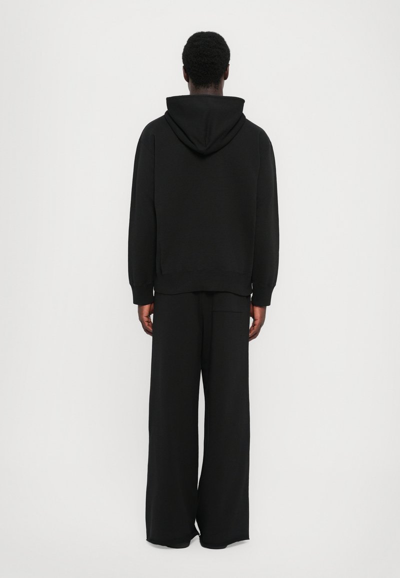 Sudadera con capucha negra de corte relajado, combinada con pantalones negros de pernera ancha. Ambos artículos están confeccionados con una suave tela texturizada.