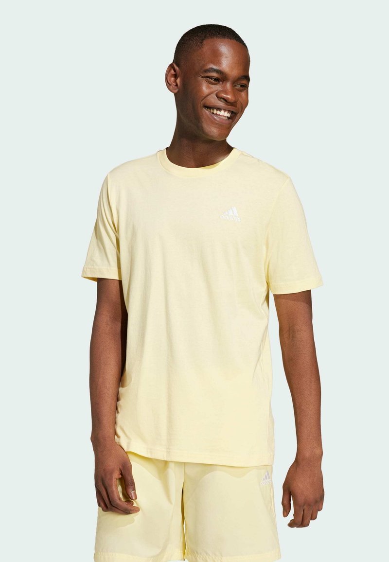 Camiseta de algodón de color amarillo claro con mangas cortas y un escote redondo. Presenta un pequeño logo blanco de adidas en el pecho.