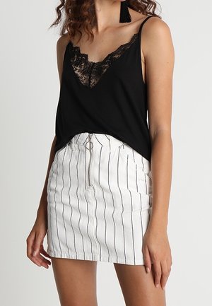 Vrouw draagt een zwart kanten hemdje met versieringen en een witte minirok met verticale zwarte strepen en een ritssluiting aan de voorkant.