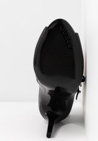 Czarna szpilka z ostro zakończonym noskiem i błyszczącą, gładką powierzchnią. Posiada teksturowaną, żłobioną podeszwę oraz wytłoczone logo.