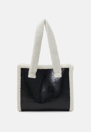 Sort rektangulær håndtaske med hvidt fluffy kantbånd og håndtag, tekstureret skinnende overflade, vist mod en ensfarvet hvid baggrund.