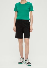 Grön bomullströja med rund halsringning, tillsammans med svarta shorts med knappstängning. Bärs med vita sneakers med gröna detaljer.