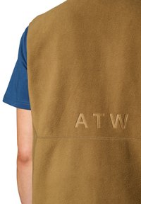 Bruine fleece vest met een gladde textuur, met verhoogde letters "ATW" op de achterkant. Draagt over een blauw shirt met korte mouwen.