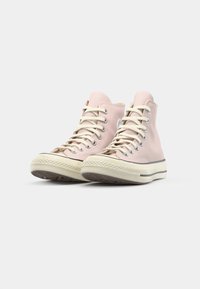 Rosa canvas høytop sneakers med kremfargede snøring og kant, med gummisåler og en logo-patch på den ytre siden.