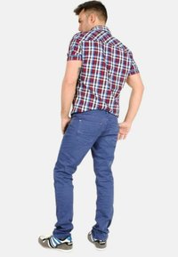 Camisa de cuadros de manga corta para hombre en rojo, azul y blanco, combinada con pantalones chinos azules y zapatos negros con rayas azules y blancas.