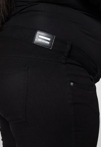 Jeans de ganga pretos com uma textura suave, um patch de couro com a marca na parte de trás e um design de bolso tradicional com pormenores metálicos.