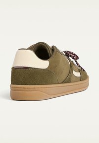 Baskets en daim vert avec un accent en cuir beige, surface texturée, bout rond et lacets bordeaux à motifs. Semelle en caoutchouc à finition lisse.