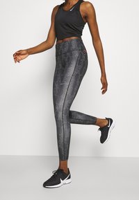 Schwarze sportliche Leggings mit Musterdesign, hohem Bund und glatter Textur, kombiniert mit einem schwarzen ärmellosen Oberteil und schwarzen Turnschuhen.